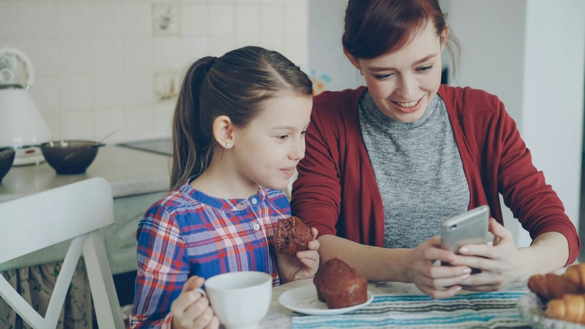 Parent and child sitting on a sofa looking at a smartphone together