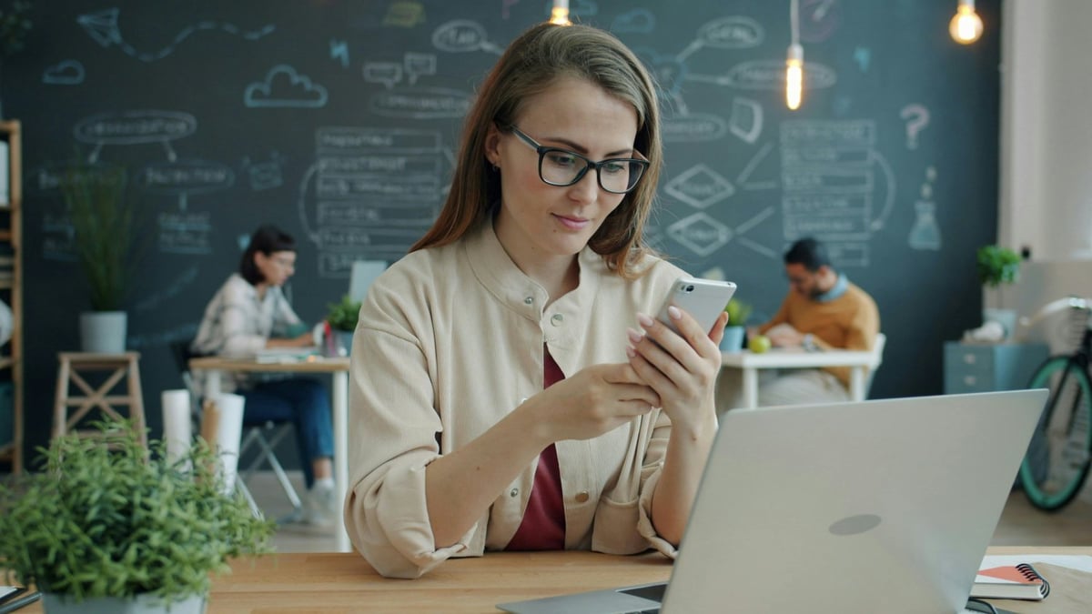 Woman using smartphone and laptop to manage social selling messages and payments